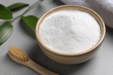 Bamboo toothbrush, green leaf and bowl of baking soda on grey table, closeup