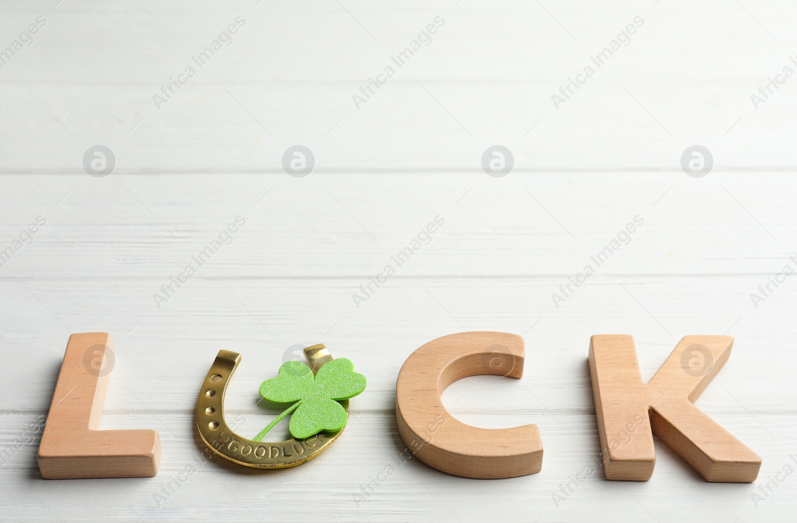 Photo of Word LUCK made of wooden letters and horseshoe on white table, space for text