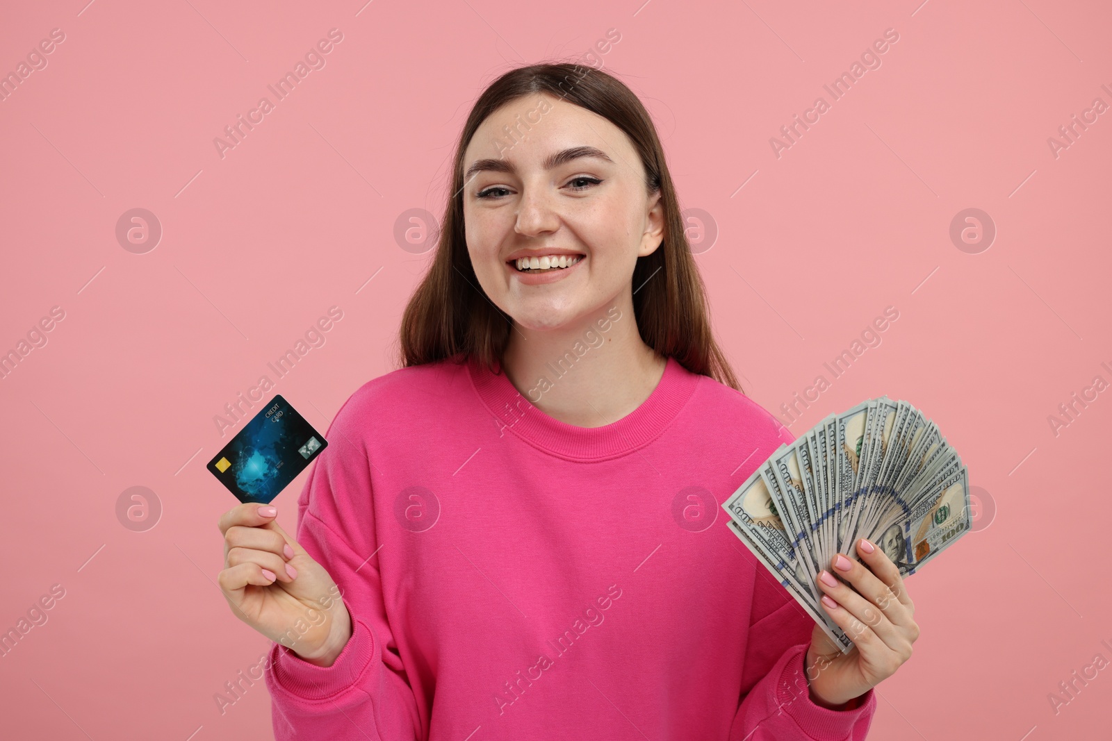 Photo of Happy woman with credit card and dollar banknotes on pink background