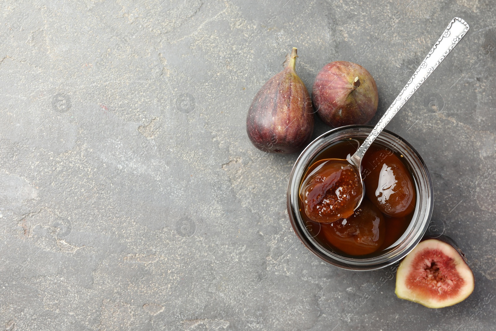 Photo of Jar of tasty sweet jam and fresh figs on grey table, flat lay. Space for text