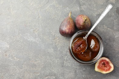 Photo of Jar of tasty sweet jam and fresh figs on grey table, flat lay. Space for text