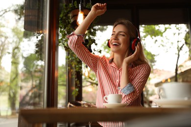 Photo of Young woman with headphones listening to music in cafe