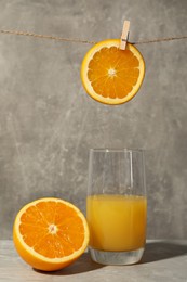 Photo of Glass of tasty orange juice and cut fruit on grey table