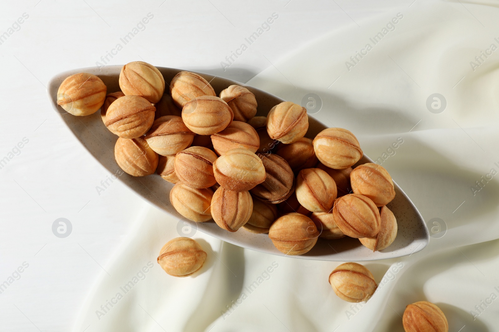 Photo of Freshly baked walnut shaped cookies on white table, top view. Homemade pastry filled with caramelized condensed milk