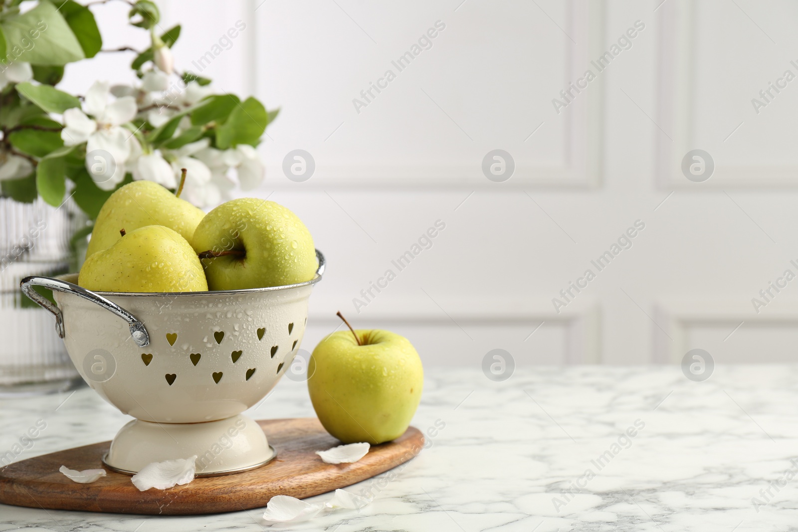 Photo of Colander with fresh apples and flower petals on white marble table, space for text