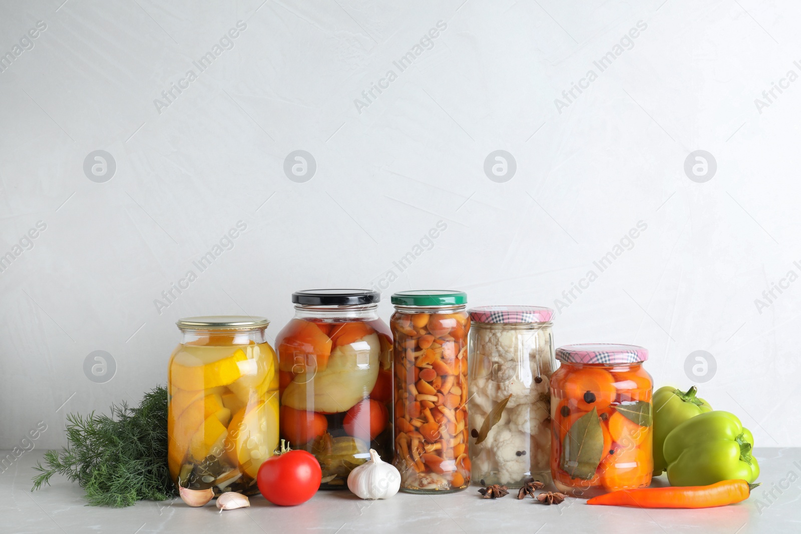 Photo of Fresh vegetables and jars of pickled products on light grey table