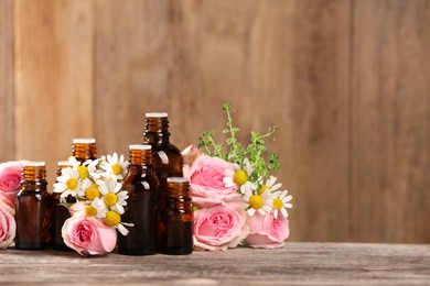 Photo of Bottles with essential oils, thyme and flowers on wooden table. Space for text