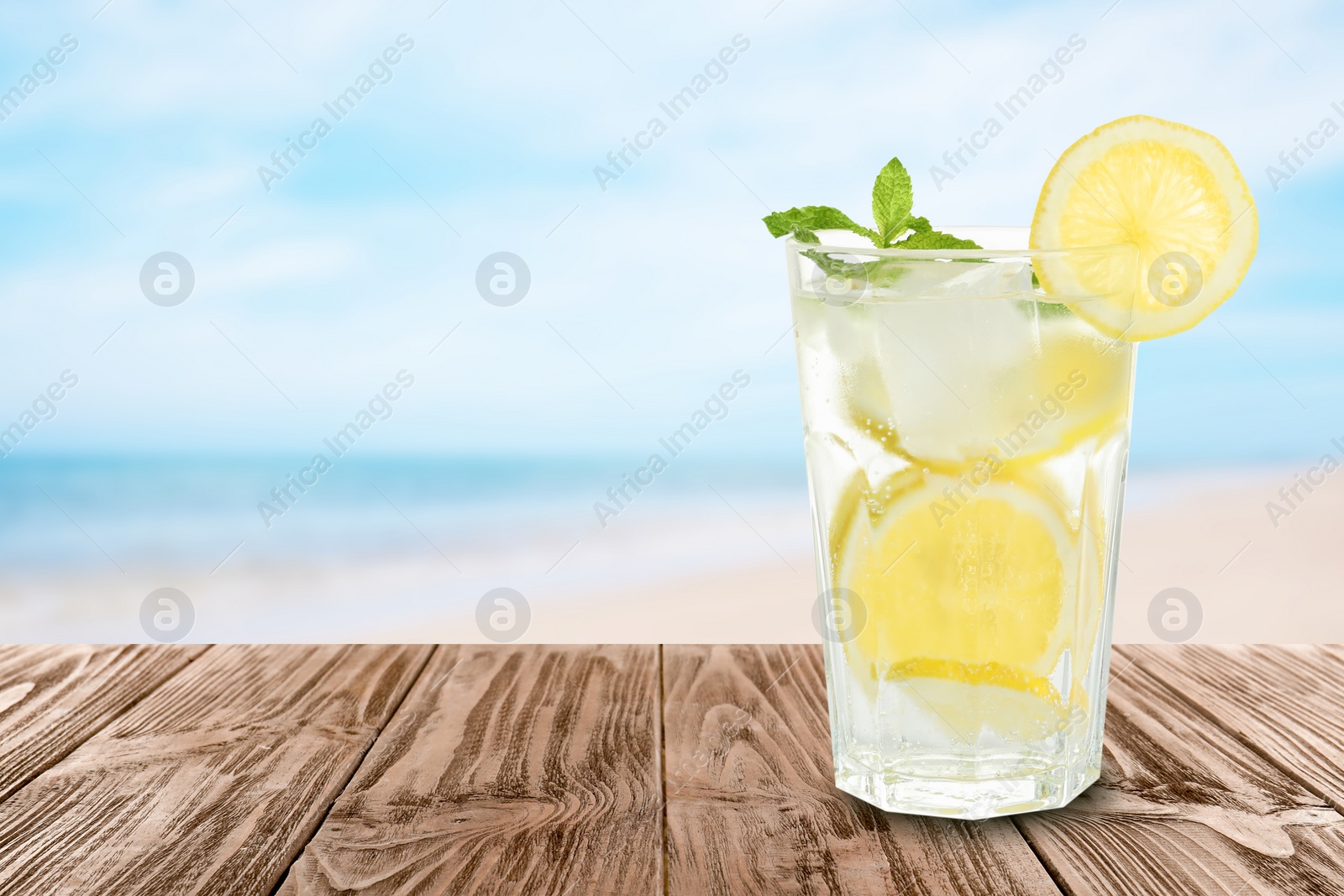 Image of Lemonade with mint and ice cubes on wooden table at beach, space for text