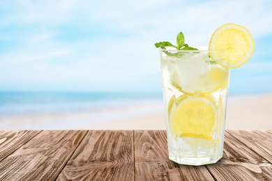 Lemonade with mint and ice cubes on wooden table at beach, space for text