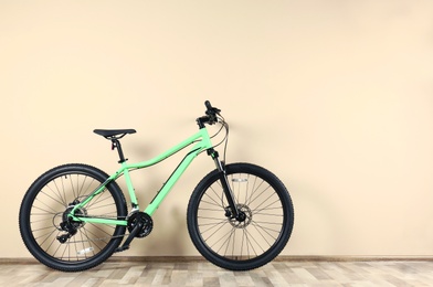 Photo of Modern bicycle near beige wall indoors. Space for text