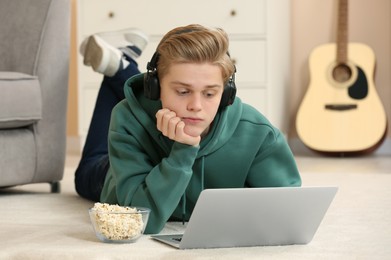 Teenage boy with headphones and popcorn using laptop at home