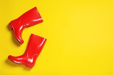 Photo of Pair of red rubber boots on yellow background, top view. Space for text
