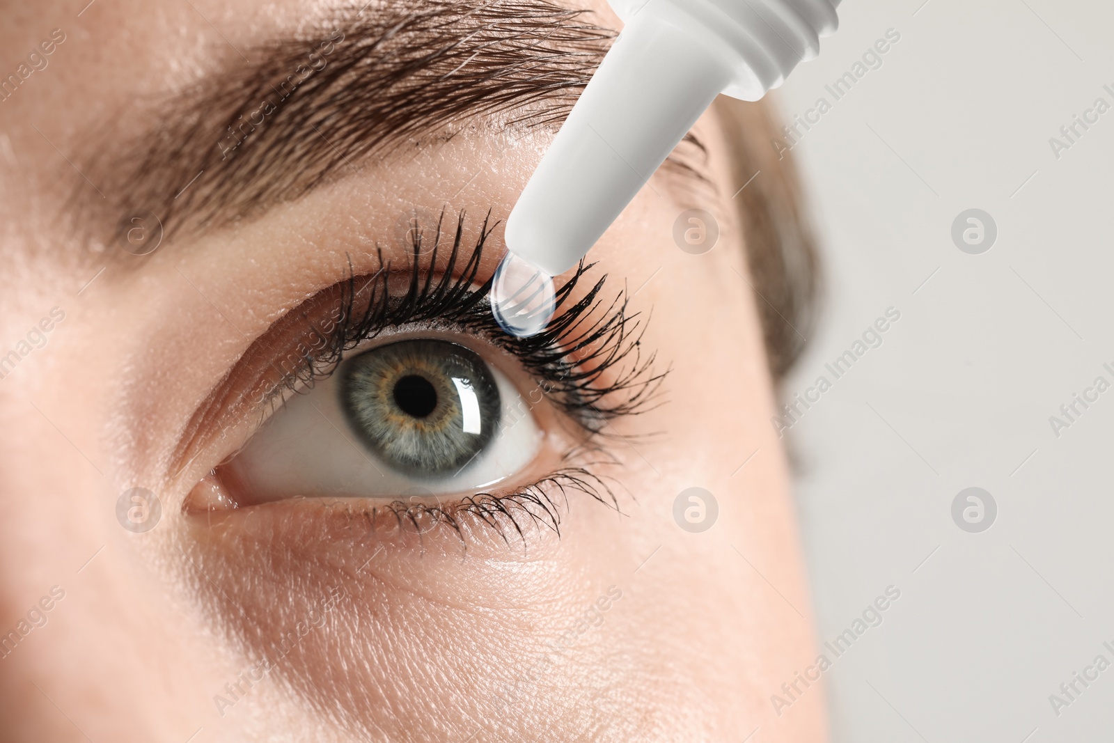 Image of Woman applying eye drops on light background, closeup