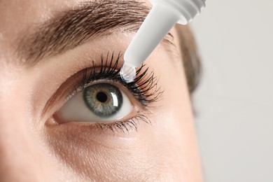 Woman applying eye drops on light background, closeup