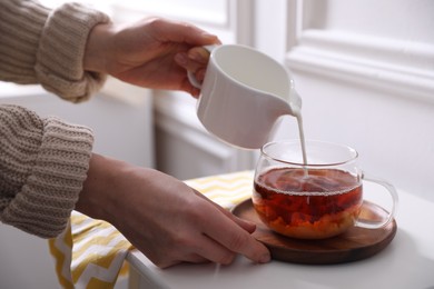 Photo of Woman pouring milk into cup of tea at white table, closeup