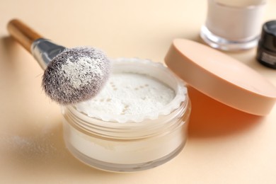 Makeup brush with rice loose face powder on beige background, closeup