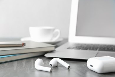 Photo of Earphones, charging case, notebooks and laptop on grey table