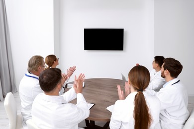 Photo of Team of doctors watching presentation on tv screen in room. Medical conference