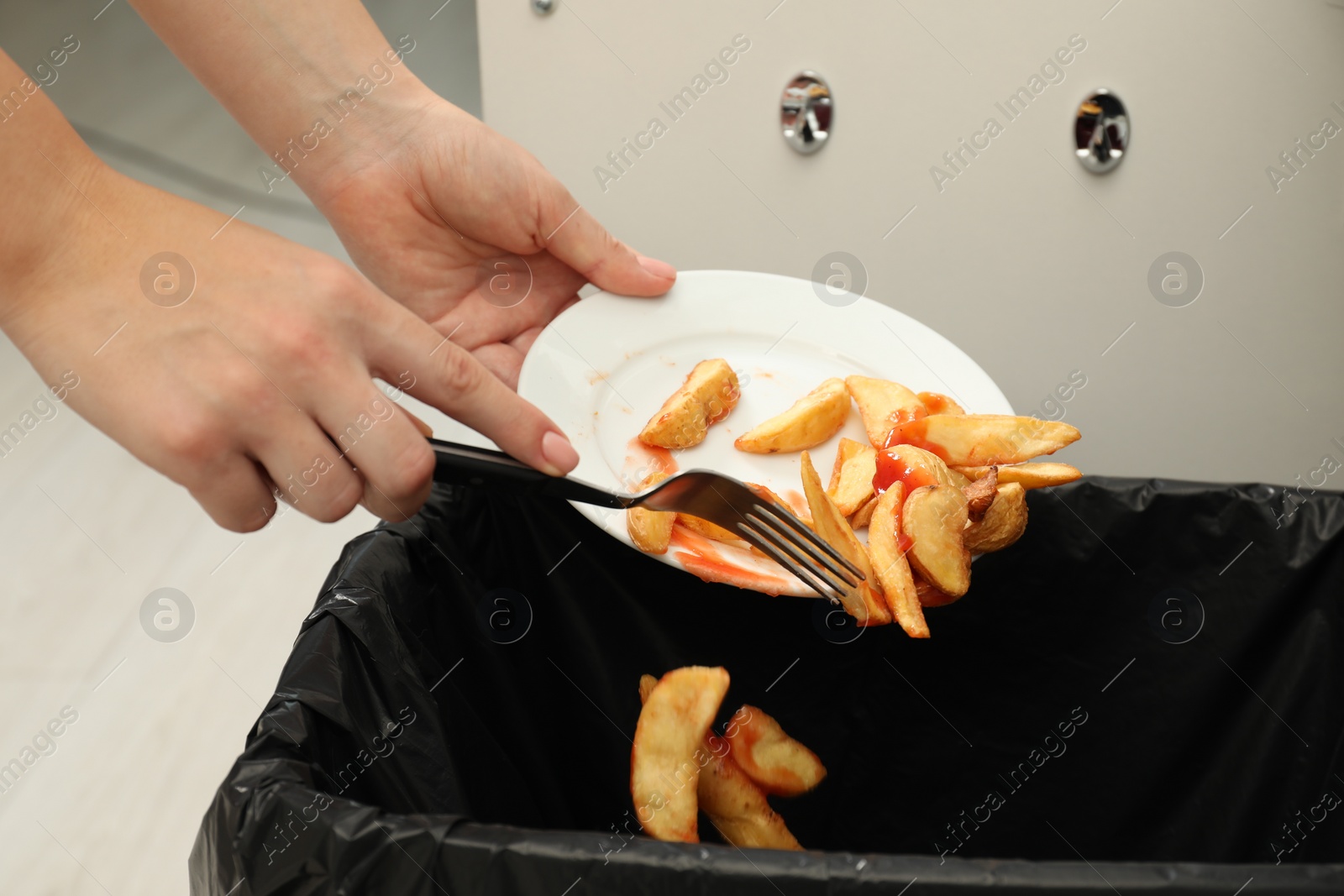 Photo of Woman throwing baked potato with ketchup into bin indoors, closeup