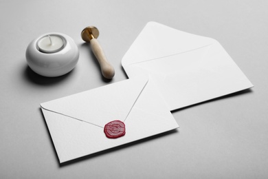 Photo of Envelopes with wax seal, candle and stamp on grey background
