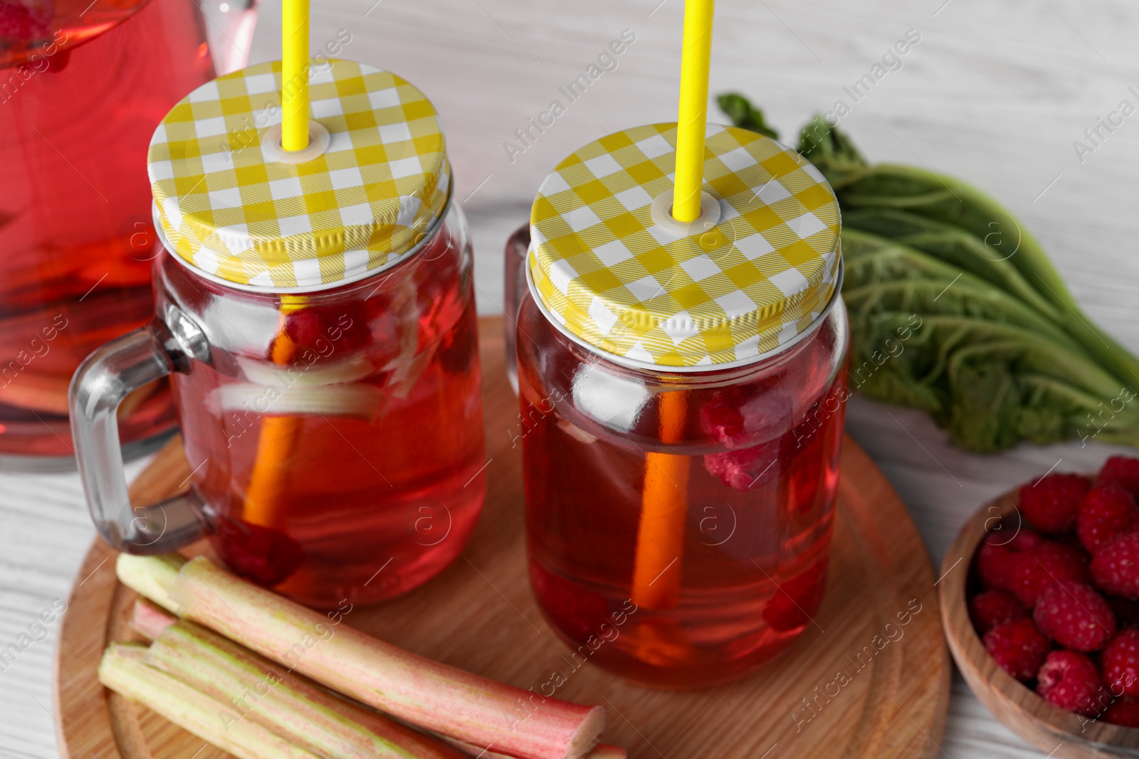 Photo of Mason jars of tasty rhubarb cocktail with raspberry and stalks on white table