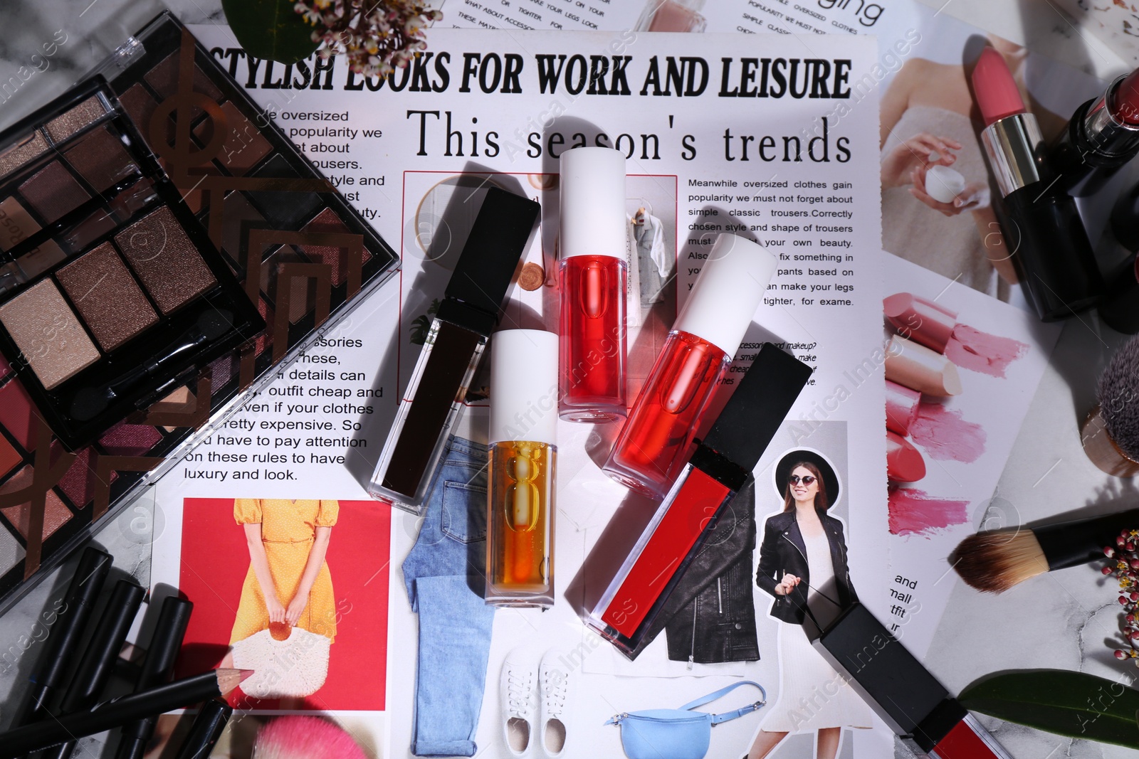 Photo of Bright lip glosses among different cosmetic products and fashion magazine on table, flat lay