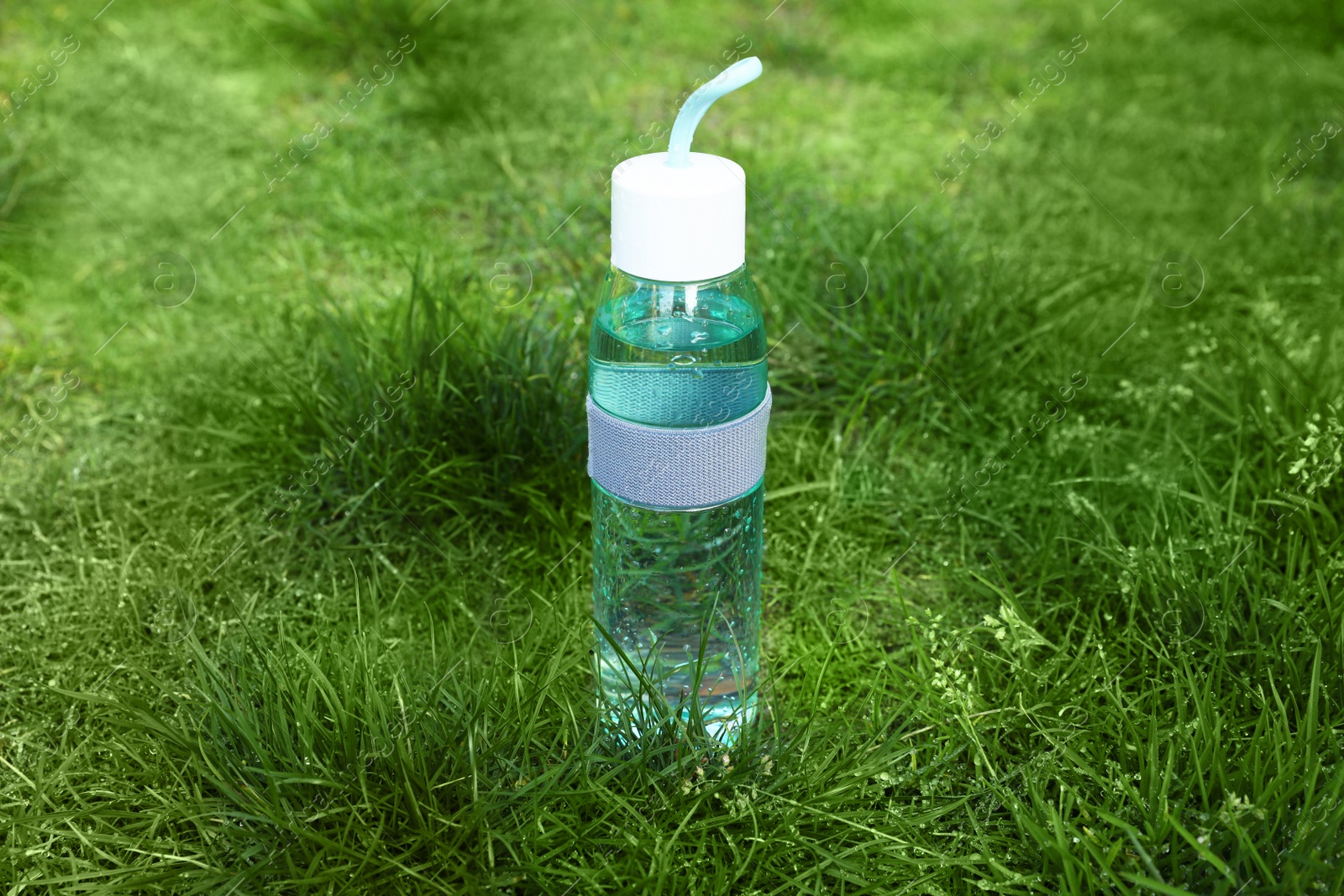 Photo of Glass bottle of fresh water on green grass outdoors