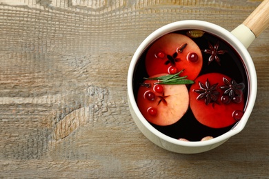 Saucepan with tasty mulled wine on wooden background, top view. Space for text