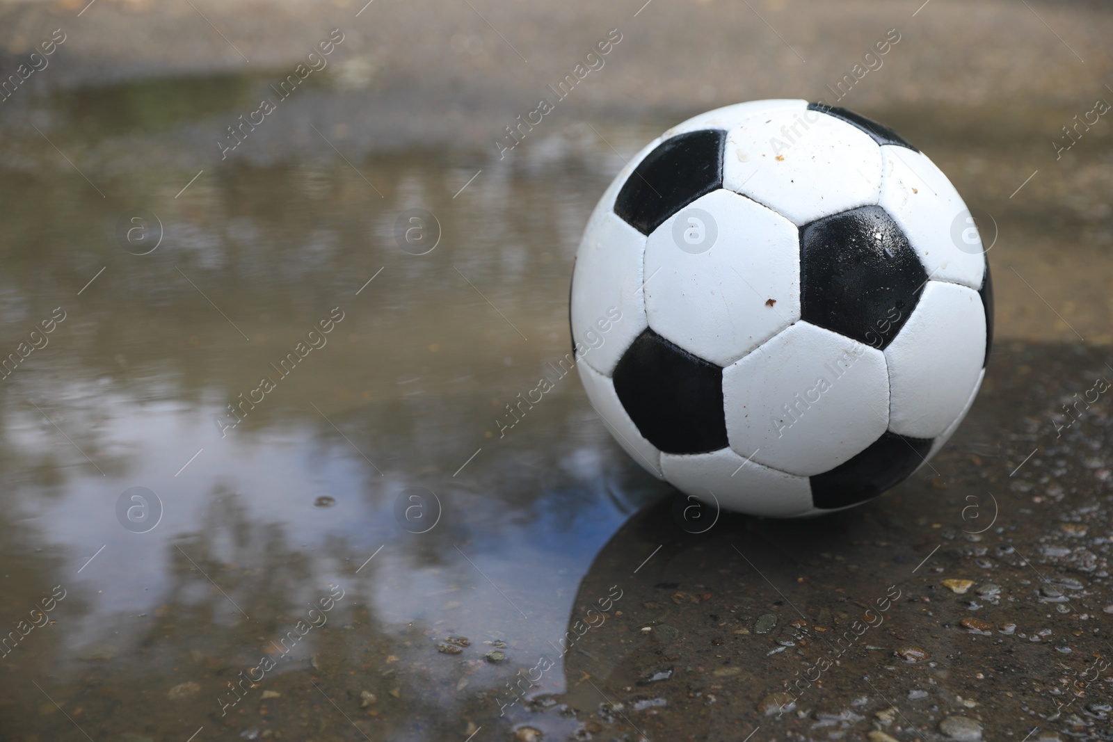 Photo of Soccer ball near puddle outdoors, space for text