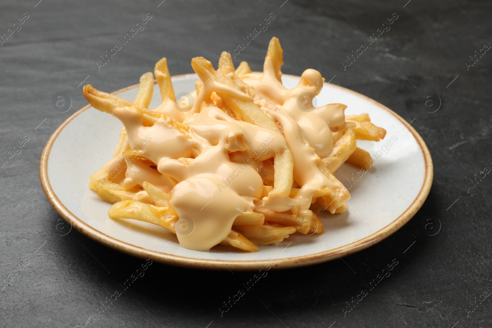 Photo of Delicious French fries with cheese sauce on black table, closeup