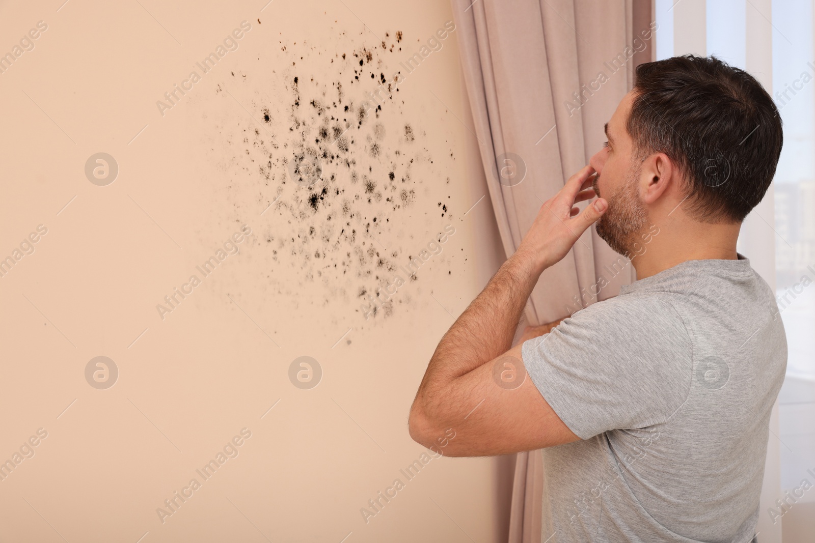 Image of Shocked man looking at affected with mold wall in room