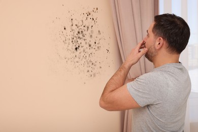 Image of Shocked man looking at affected with mold wall in room