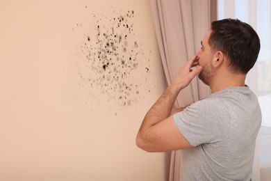 Shocked man looking at affected with mold wall in room