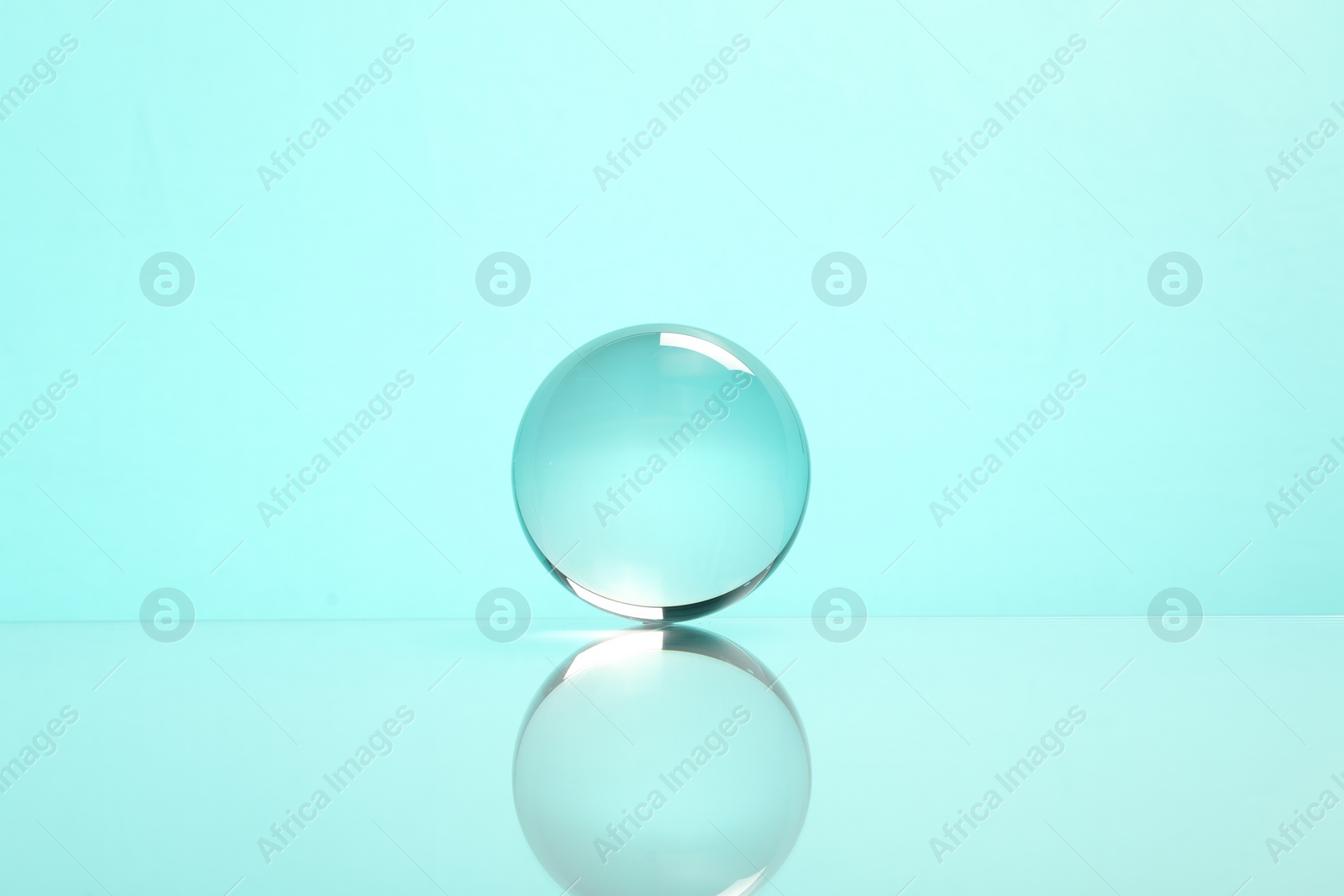 Photo of Transparent glass ball on mirror surface against turquoise background