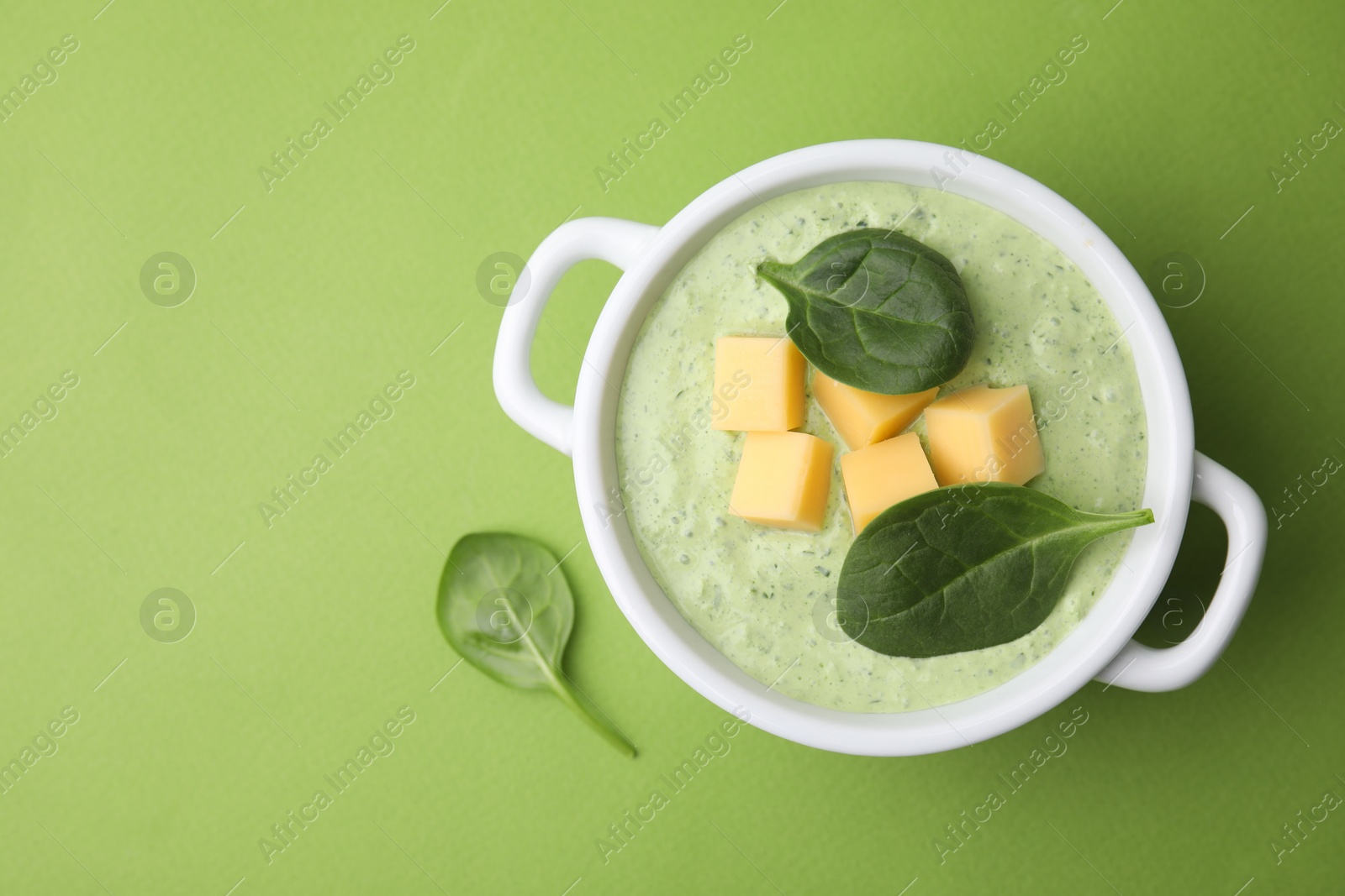 Photo of Delicious spinach cream soup with cheese in bowl on green background, top view. Space for text