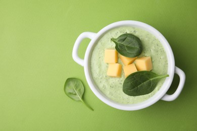 Delicious spinach cream soup with cheese in bowl on green background, top view. Space for text