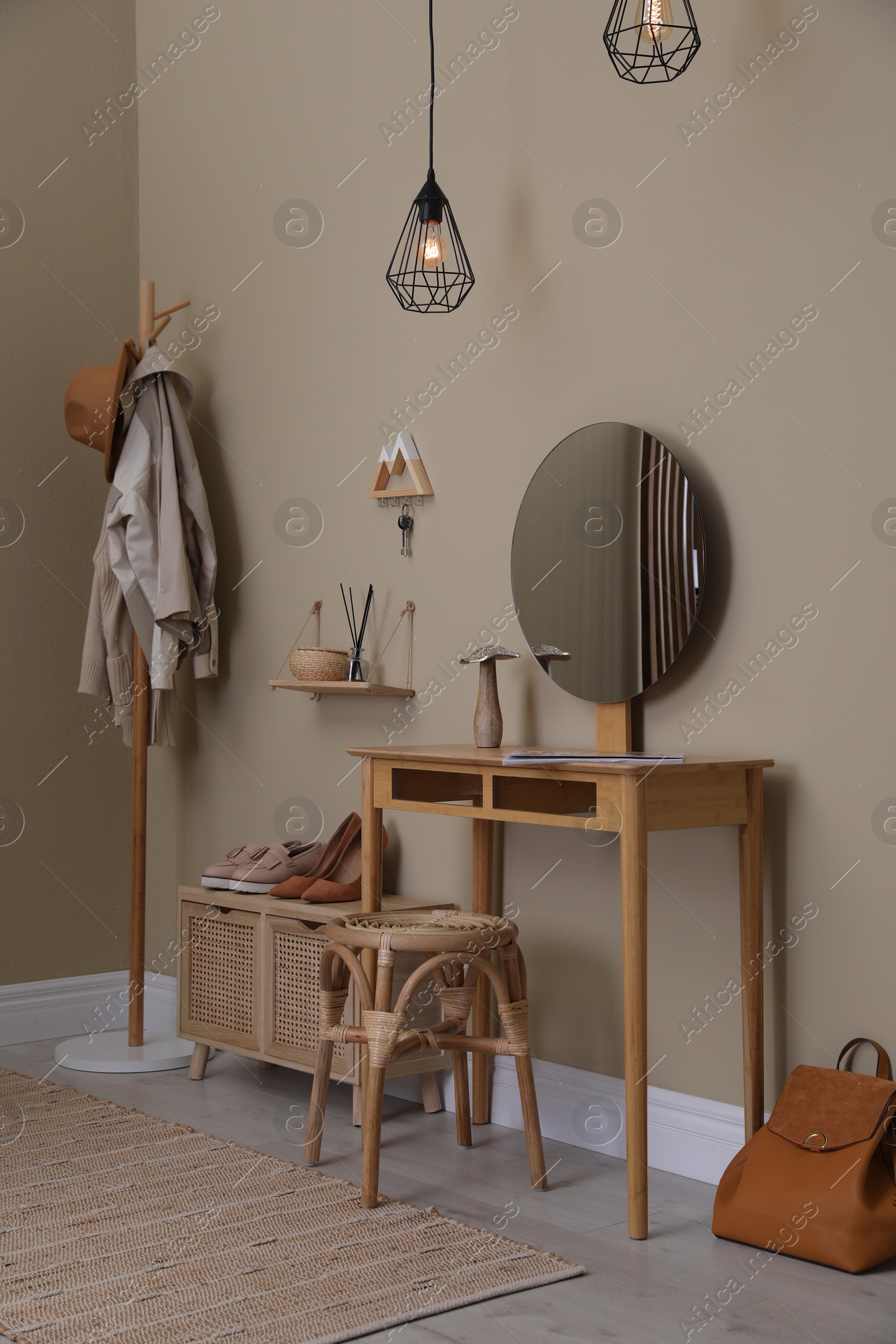 Photo of Modern hallway interior with stylish furniture, round mirror and wooden hanger for keys on beige wall