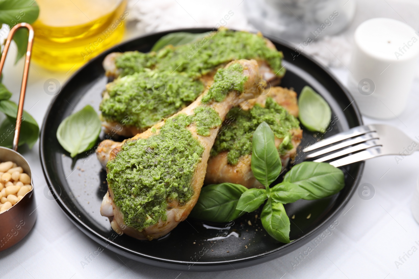 Photo of Delicious fried chicken drumsticks with pesto sauce, ingredients and fork on white table, closeup