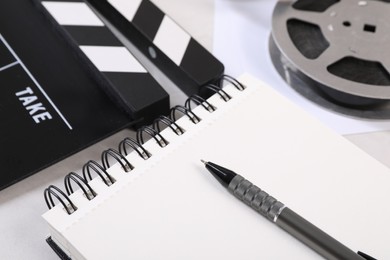 Movie clapper, film reel, notebook and pen on light table, closeup