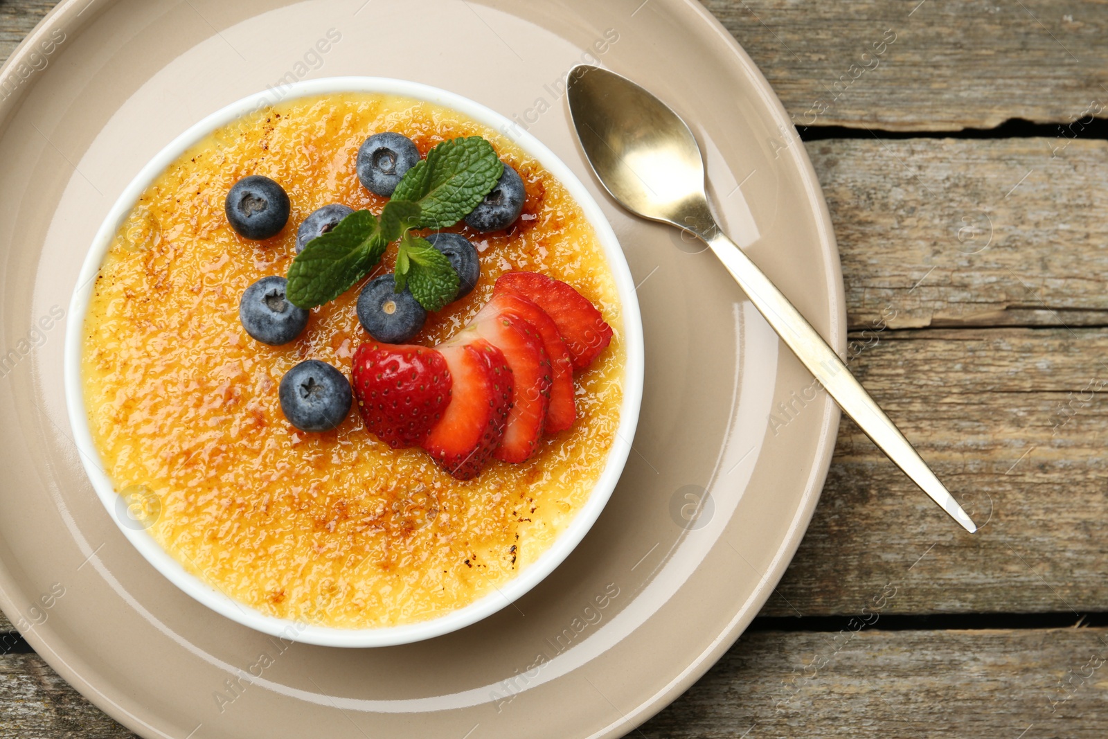 Photo of Delicious creme brulee with berries and mint in bowl on wooden table, top view