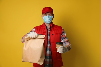 Courier in protective mask and gloves holding order on yellow background. Food delivery service during coronavirus quarantine