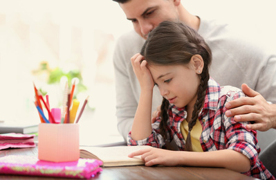 Photo of Man helping his daughter with homework at table indoors