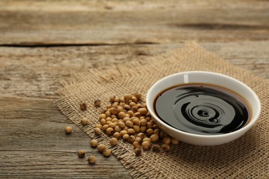 Photo of Soy sauce in bowl and beans on wooden table. Space for text