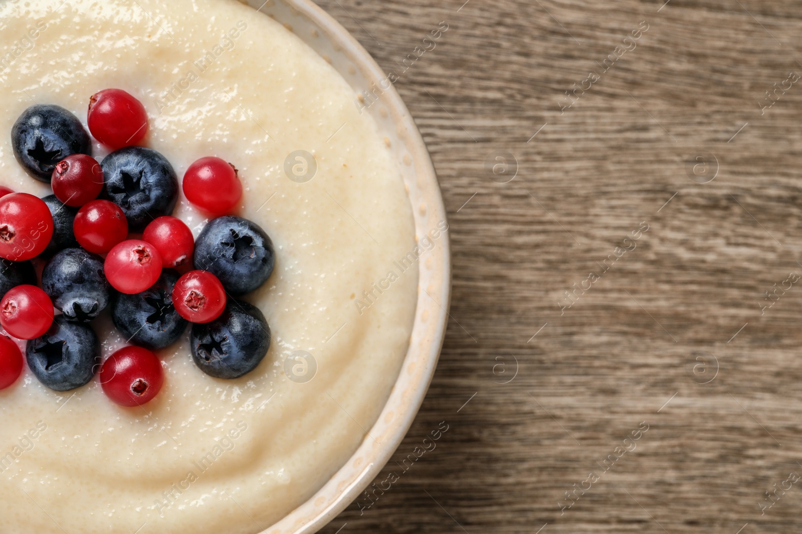 Photo of Delicious semolina pudding with berries on wooden table, top view. Space for text