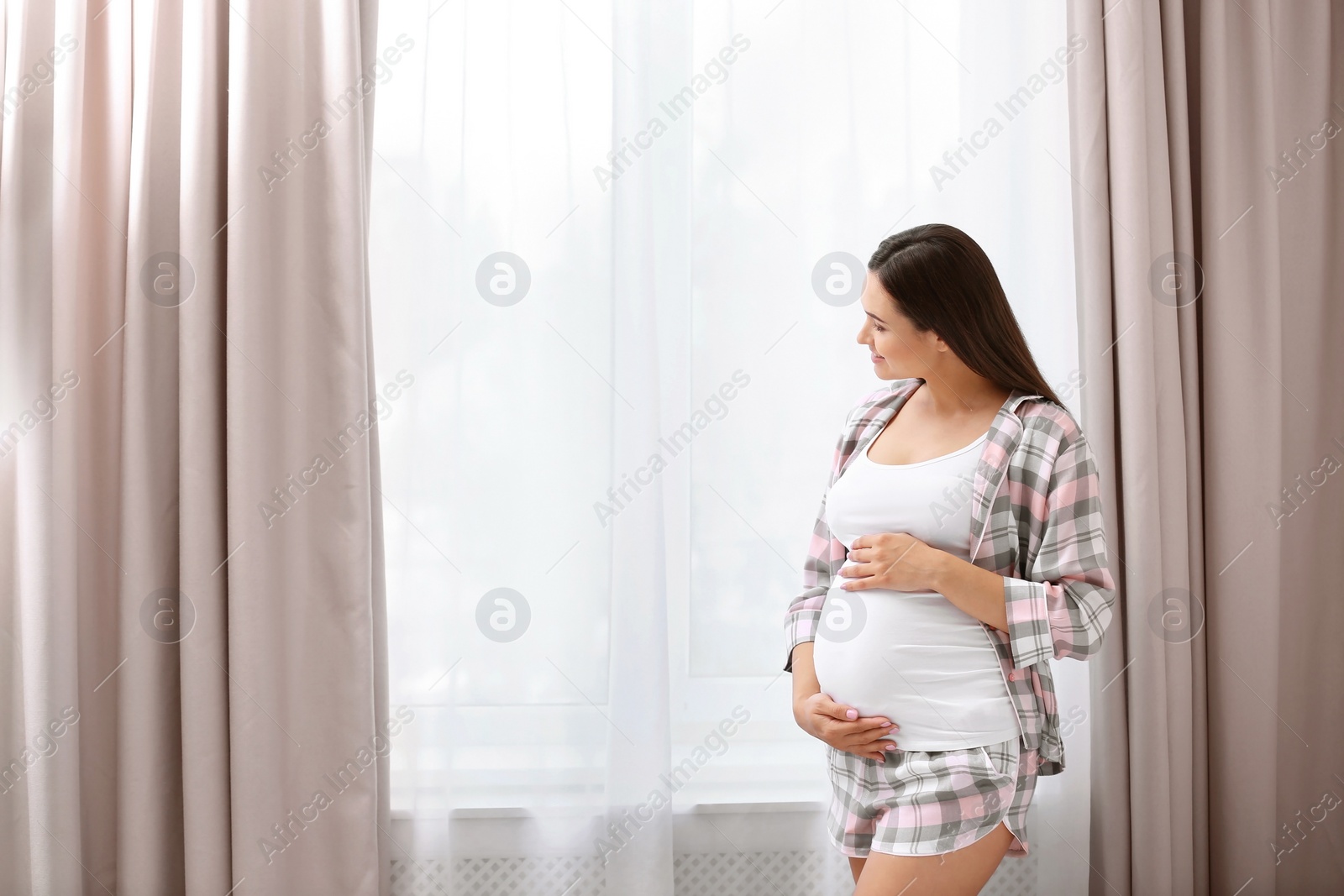 Photo of Young beautiful pregnant woman near window at home