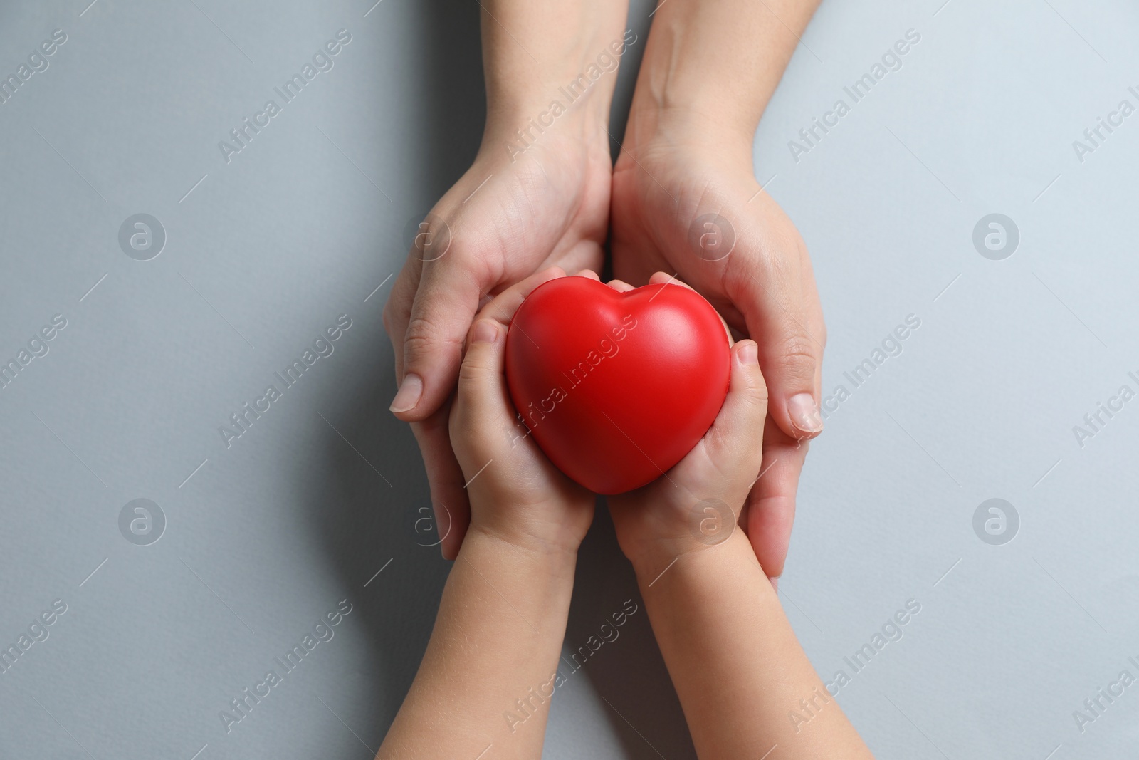 Photo of Mother and her child holding red decorative heart on gray background, top view