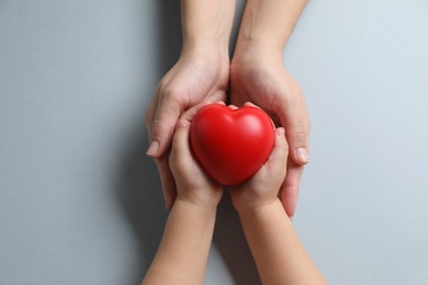 Mother and her child holding red decorative heart on gray background, top view