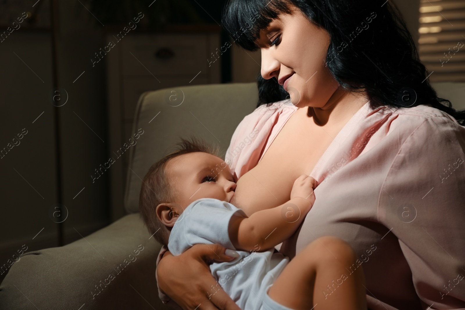 Photo of Woman breastfeeding her little baby on sofa in evening