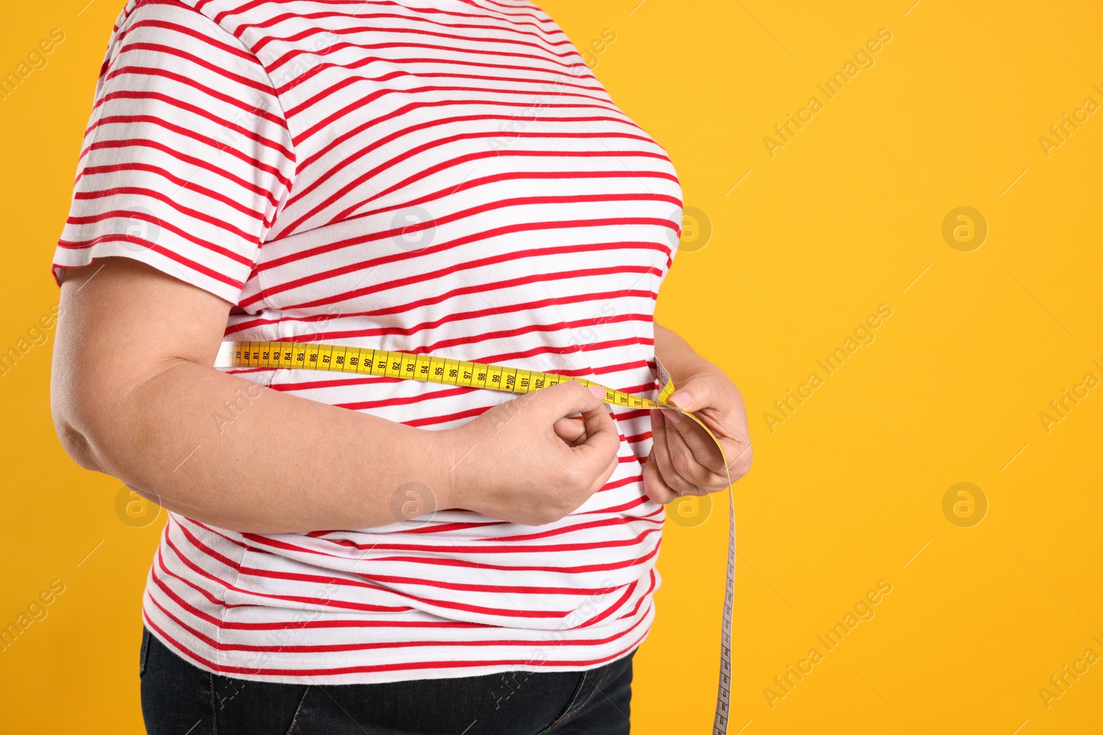 Photo of Overweight woman measuring waist with tape on orange background, closeup. Space for text