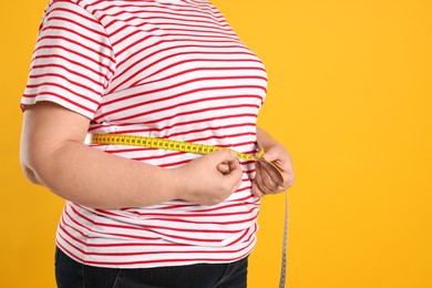 Photo of Overweight woman measuring waist with tape on orange background, closeup. Space for text